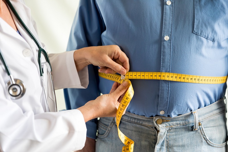 Doctor measuring man’s belly with a measuring tape