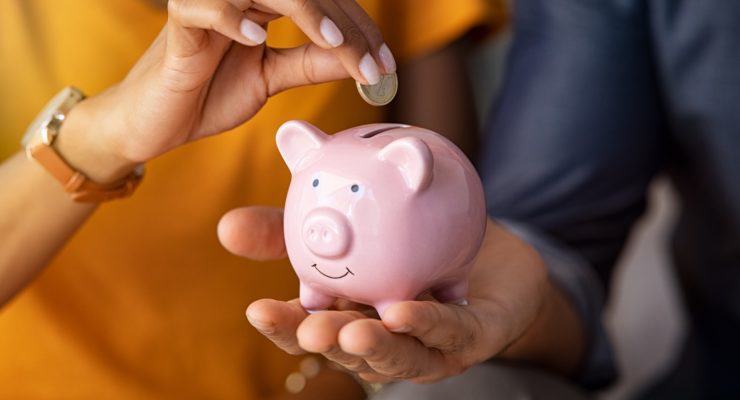 Close up of man holding pink piggy bank while woman putting coin in it.