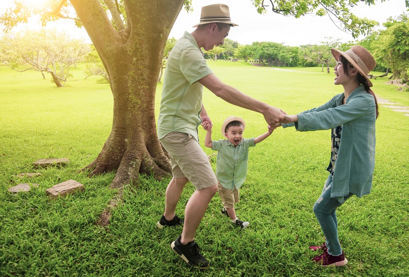 2 parents and their child holding hands dancing outdoors on green grass