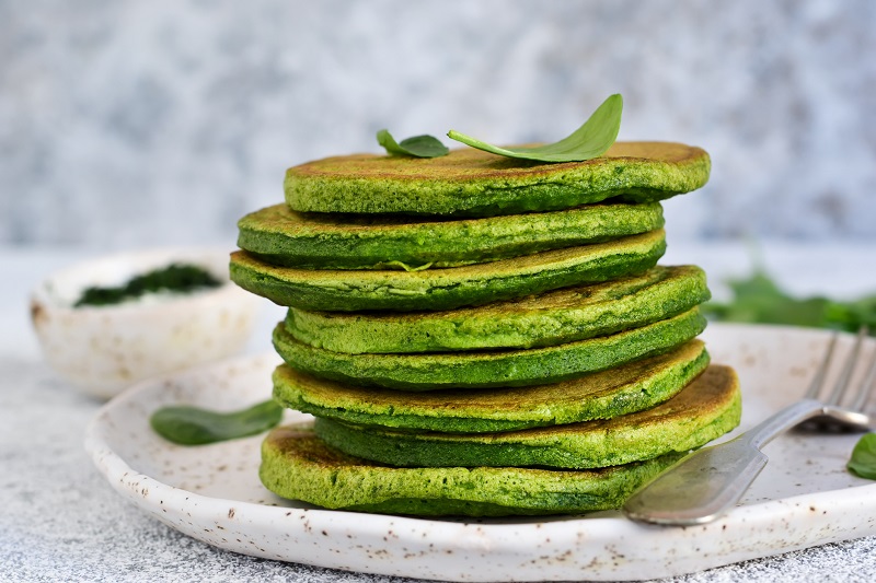 A stack of pancakes topped with spinach and banana greens