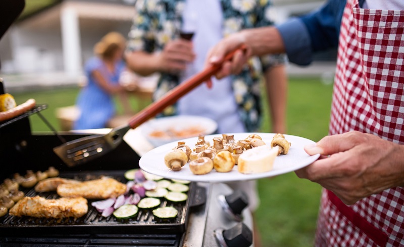 Man cooking on the grill while holding a plate with mushrooms