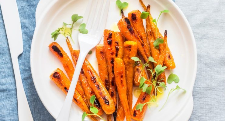 Roasted plate of baby carrots with seasoning on a white plate resting on a blue napkin