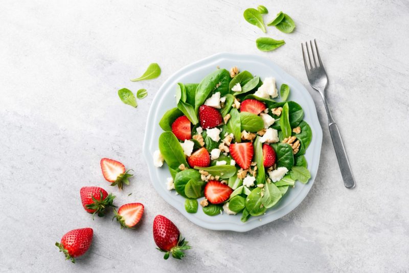 A plate of spinach strawberry and walnut salad