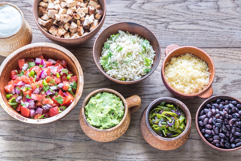 An assortment of pico de gallo, beans, and rice in bowls