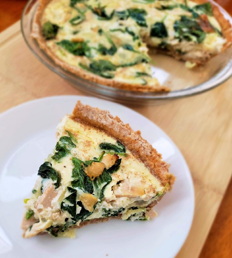 Ham and spinach quiche in a pie pan with a slice on a white plate
