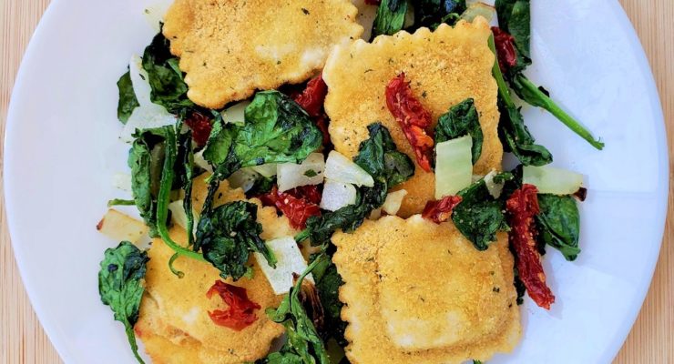toasted ravioli with spinach, onions and sun-dried tomatoes on a white plate