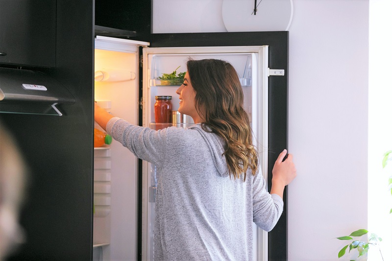 woman organizing and cleaning out her fridge to prevent food waste