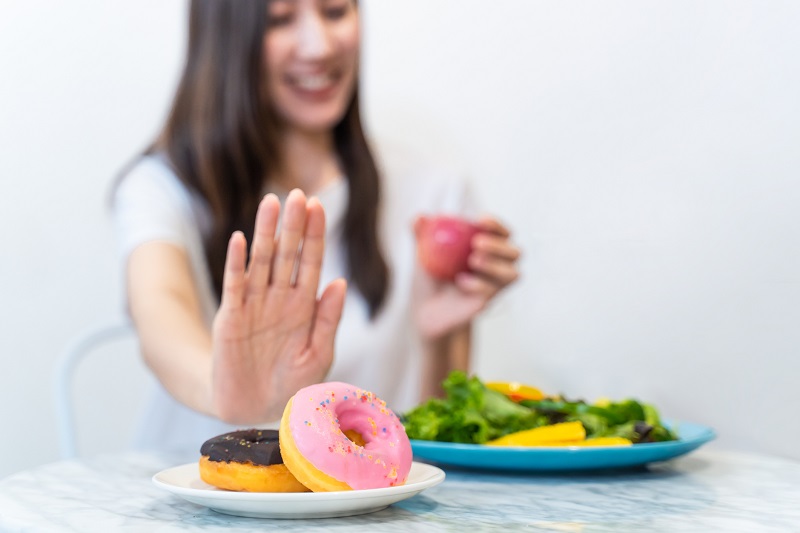 A women refusing donuts while enjoying a smoothie and salad