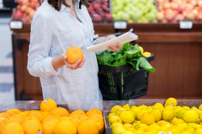 woman grocery shopping for fruit holding a basket and a shopping list