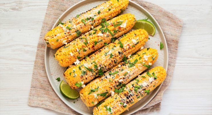 Mexican Street Corn with cheese, herbs and lime slices on a plate