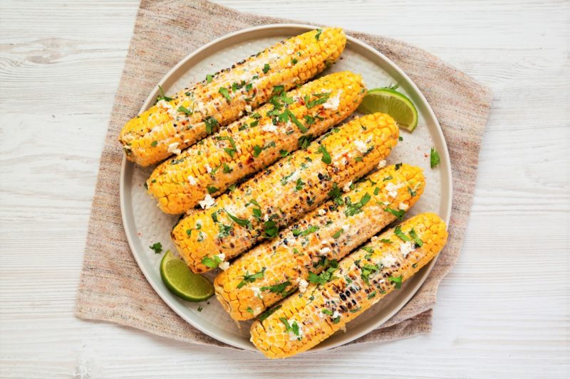 Mexican Street Corn with cheese, herbs and lime slices on a plate