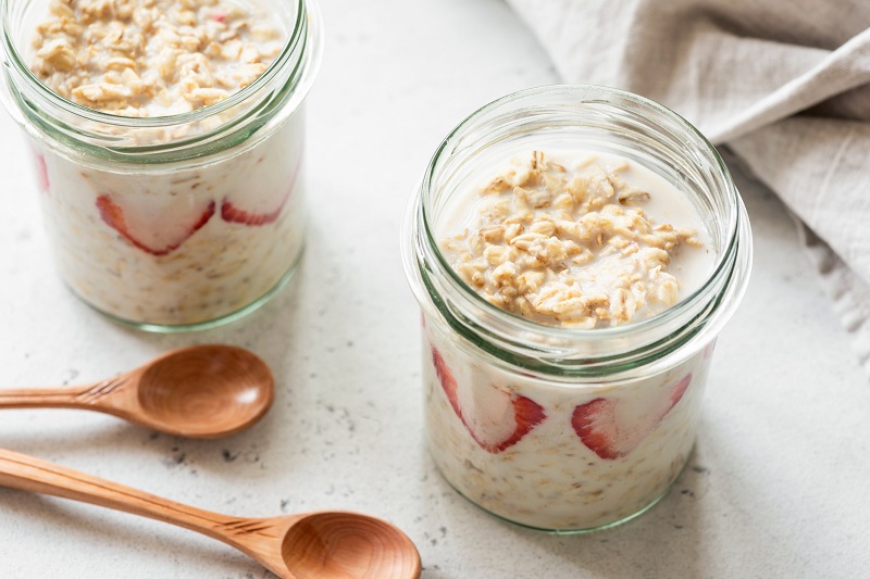 meal prepped overnight oats with strawberries in a mason jars with wooden spoons