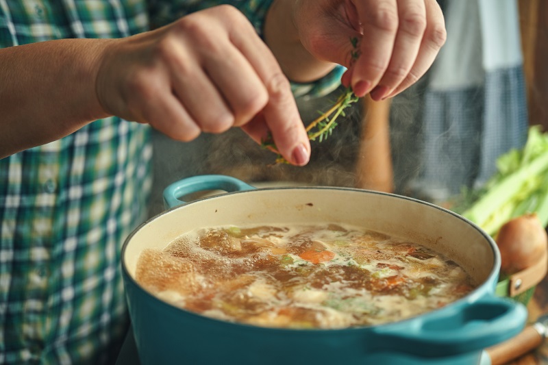 Person adding herbs to a pot of soup