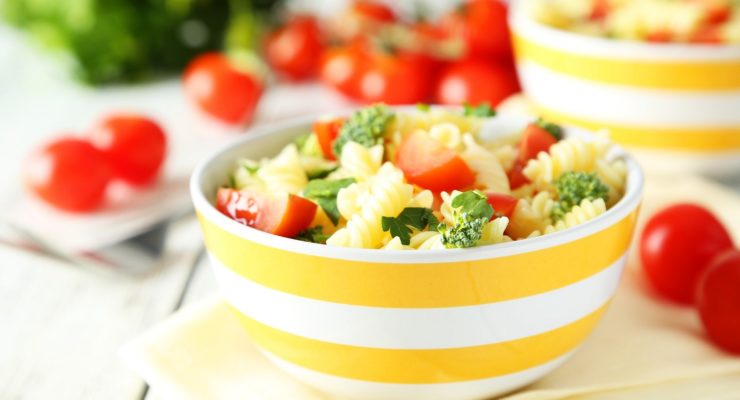summer pasta salad in a yellow striped bowl with tomatoes and broccoli