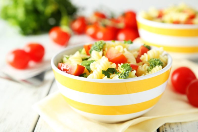 summer pasta salad in a yellow striped bowl with tomatoes and broccoli
