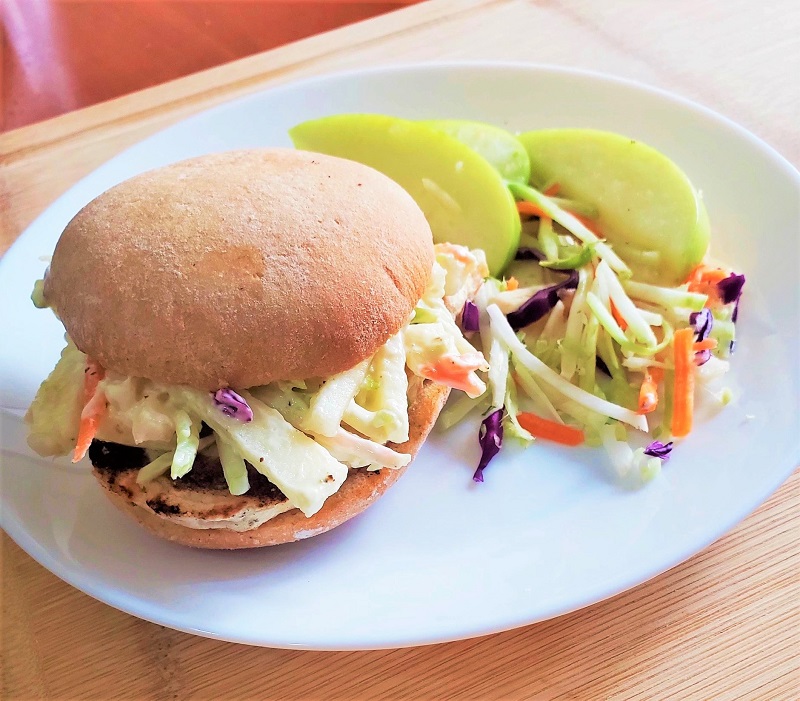 Grilled chicken sandwich with apple slaw on a white plate