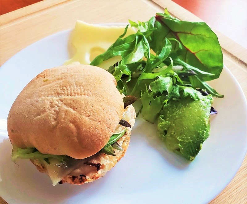 Grilled chicken sandwich with a side of greens and avocado rested on a white plate