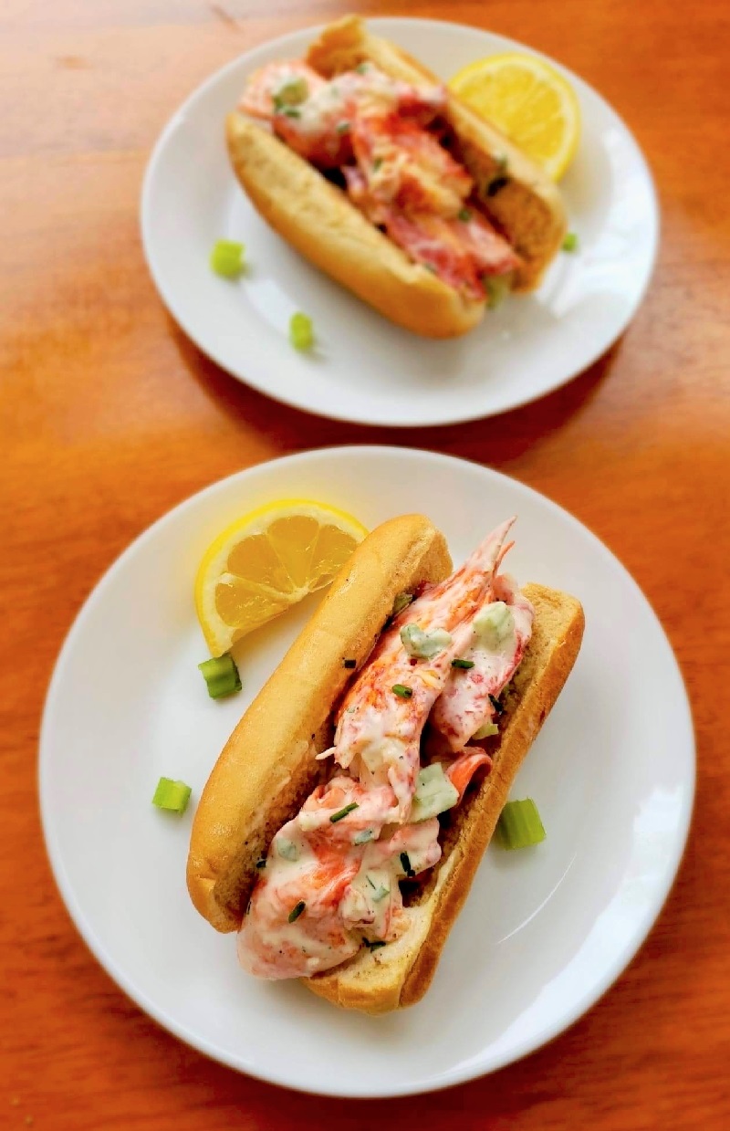 2 healthy Lobster Rolls on white plates with lemons and herbs