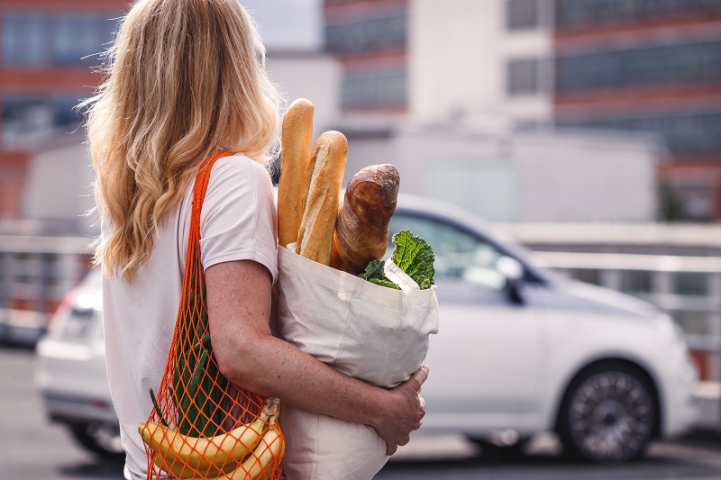 Woman with groceries walks to her car in a supermarket parking lot