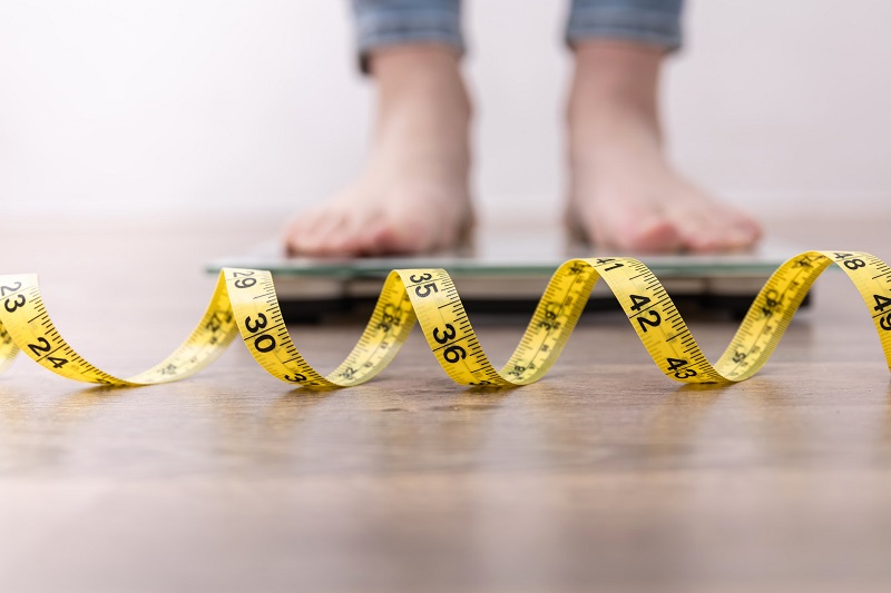 person on a scale weighing themselves with a tape measure on the floor