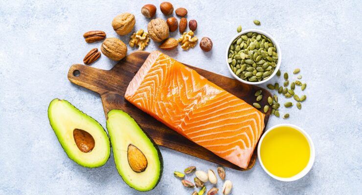 healthy fats like avocado, salmon, nuts, seeds and olive oil on a table