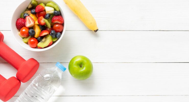 Fresh fruits salad with dumbbells sport equipment, water and banana for healthy lifestyle to boost energy naturally