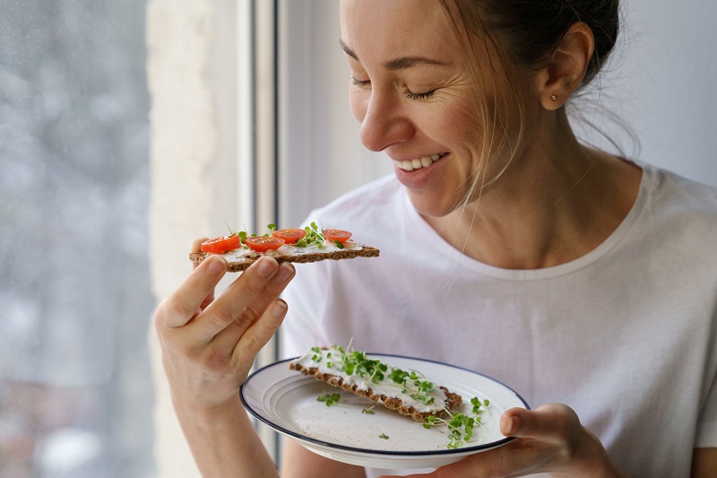 Smiling woman eating rye crisp bread with cheese and veggies