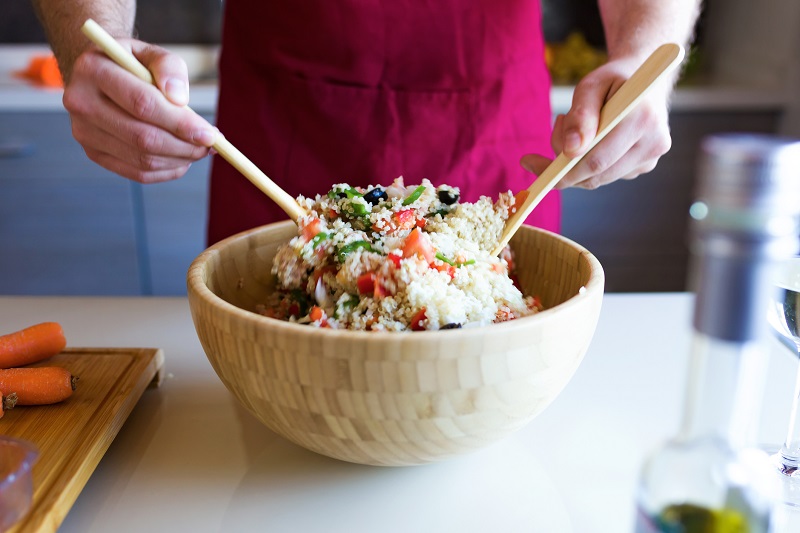 person preparing quinoa salad with vegetables 