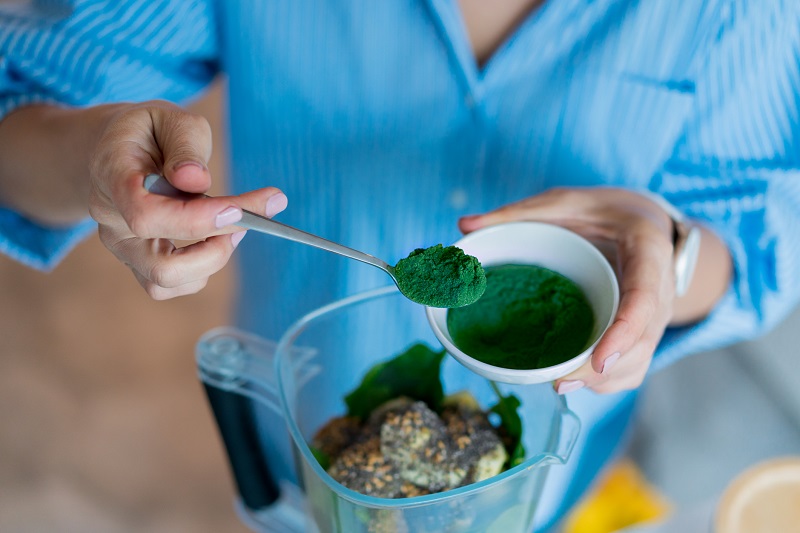 Woman adding spirulina green superfood powder to a green smoothie