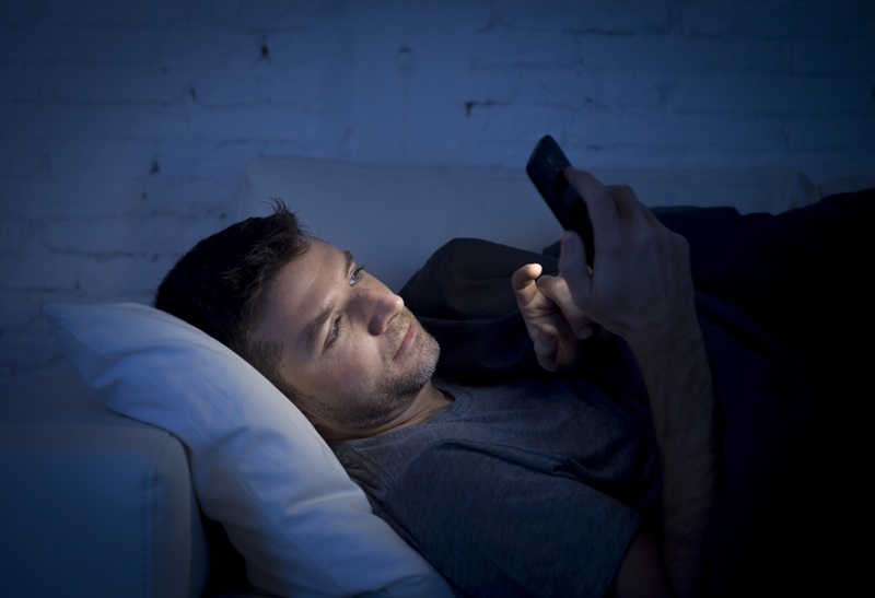 man using phone on couch looking at blue light