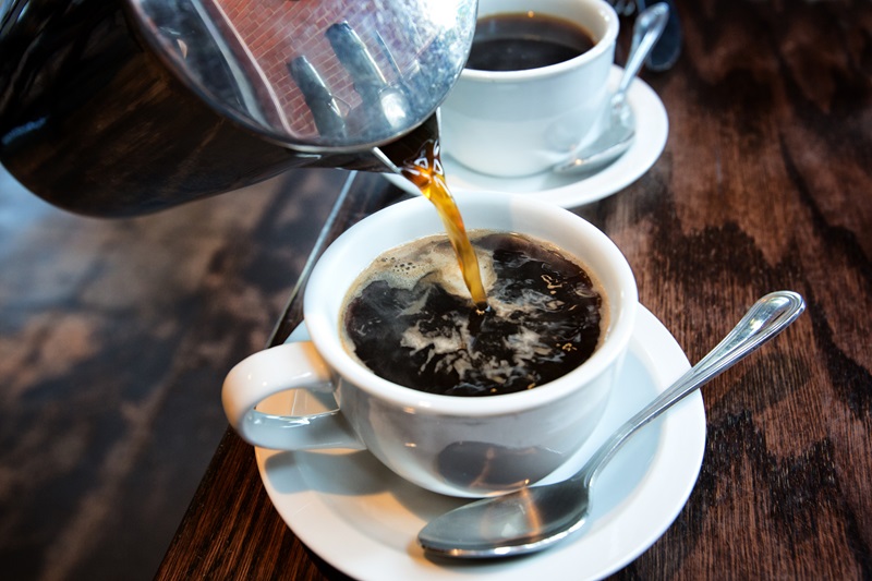 Fresh hot coffee being poured into a cup from a stainless steel french press