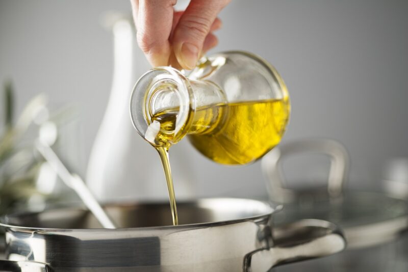 hand pouring olive oil into a cooking pot