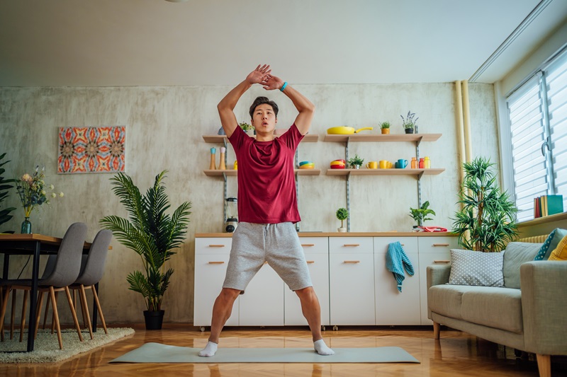 man doing exercise snacks and jumping jacks while watching TV in living room