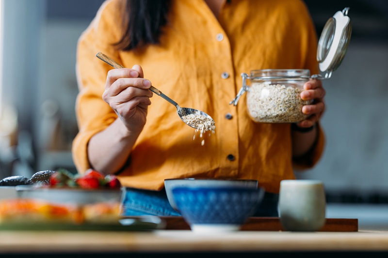 woman adding oats into a bowl meal prepping oatmeal for breakfast 