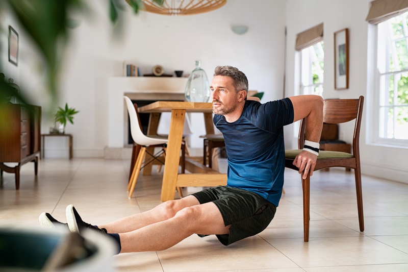 man doing fitness exercise while doing dips using chair in living room