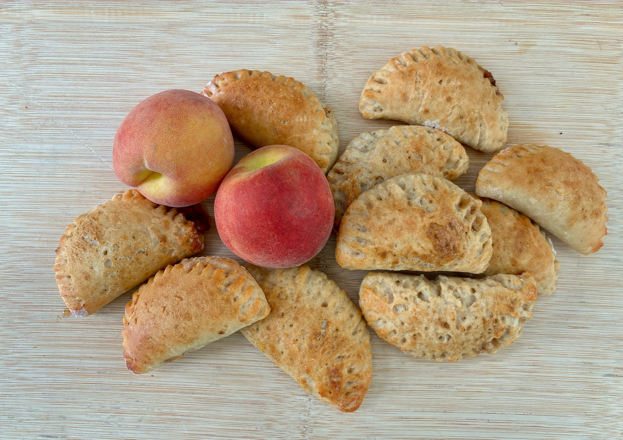 Golden-brown baked pastries and three ripe peaches on a wooden cutting board.